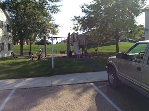 A park with a playground and a car parked in the parking lot.