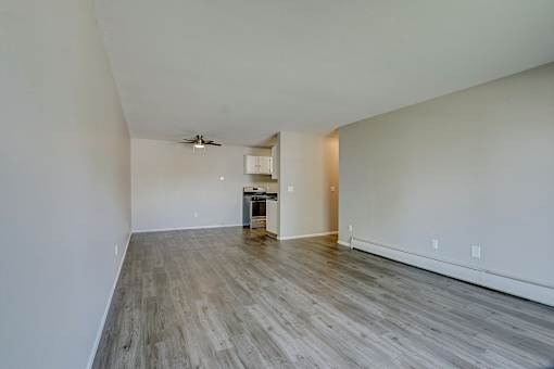 A room with a ceiling fan and a kitchenette in the corner.