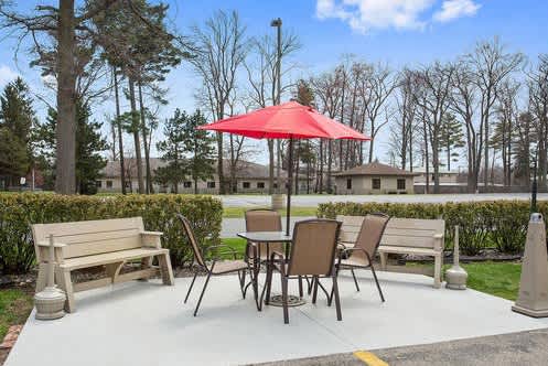 A red umbrella is on a patio table with chairs and a bench.