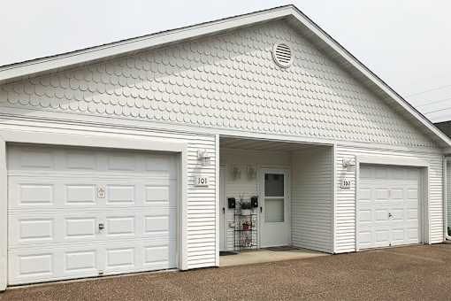 A white building with two garage doors and a wall with holes in it.