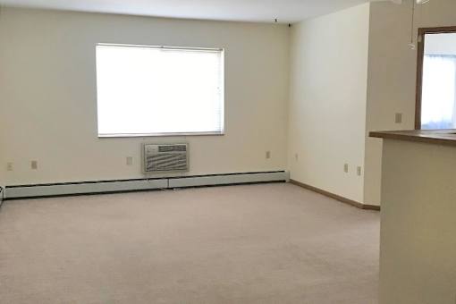 A large empty room with a window and a wall-mounted air conditioner unit.