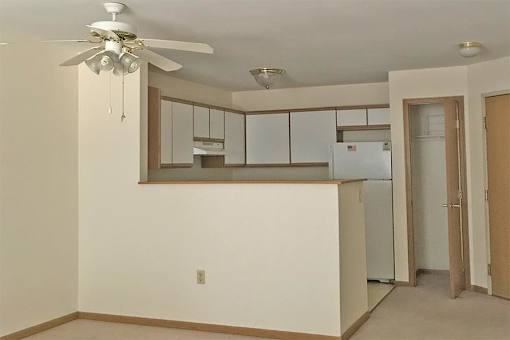 A kitchen area with a refrigerator, cabinets, and a ceiling fan.
