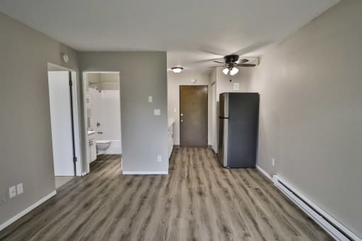 an empty living room with a refrigerator and a ceiling fan