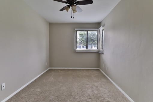 an empty bedroom with a window and a ceiling fan