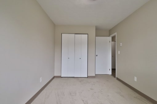 a living room with white walls and a carpet and two closets