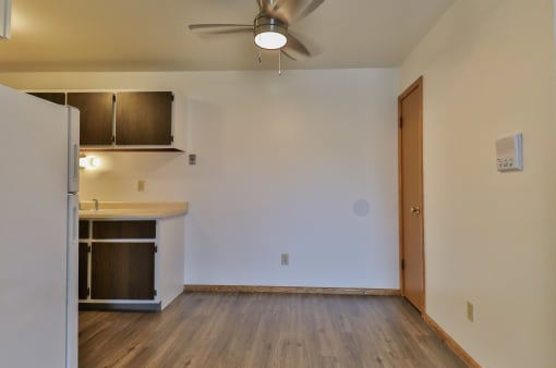 an empty living room with a kitchen and a ceiling fan