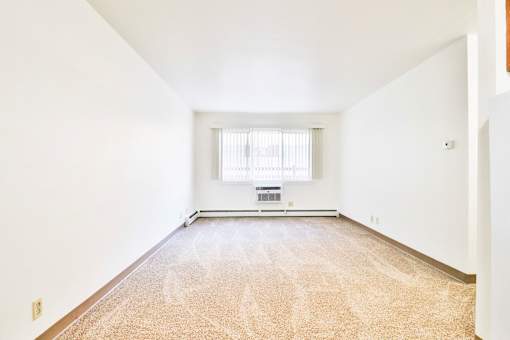 A room with a carpeted floor and a window with blinds.
