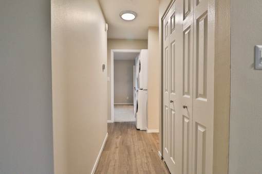 A hallway with a white door on the right and a white fridge in the middle.
