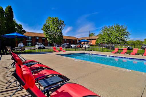 A poolside with red sun loungers and a blue umbrella.
