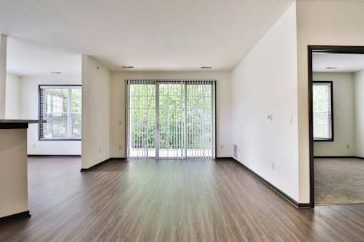 A spacious room with wooden floors and a large window with blinds.