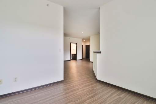 A long, empty hallway with white walls and wood flooring.