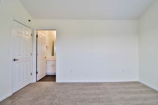 A white room with a carpeted floor and a doorway leading to another room.