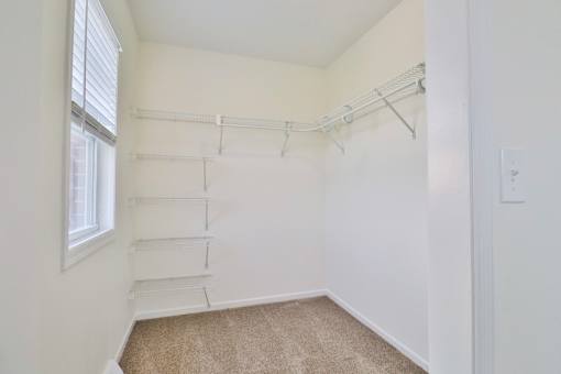 A white closet with a carpeted floor and a window.