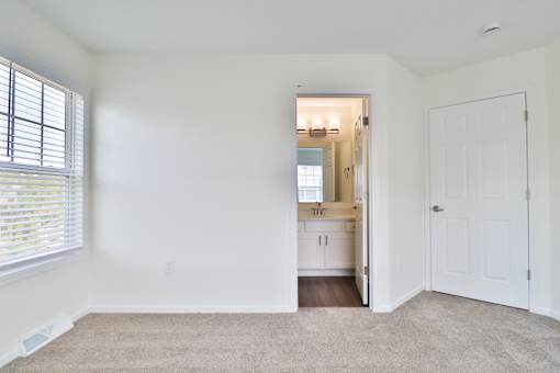A white room with a carpet and a door leading to a kitchen.