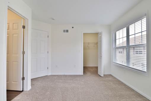 A white room with a carpeted floor and a window with blinds.