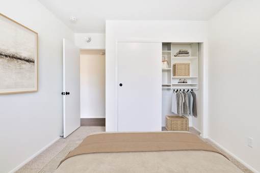 A bedroom with a bed, closet, and a painting on the wall.