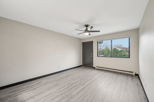 an empty living room with a window and a ceiling fan
