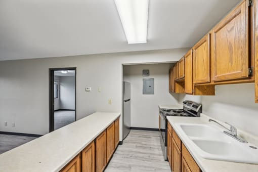 an empty kitchen with wood cabinets and white countertops and a sink and a refrigerator