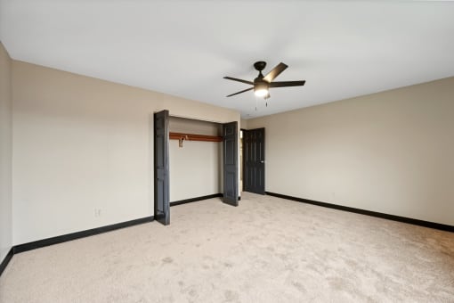 an empty living room with a ceiling fan and a door to a closet