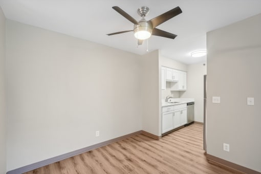an empty living room with a ceiling fan and a kitchen