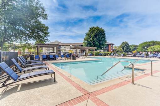 A pool with a red brick border and blue lounge chairs.