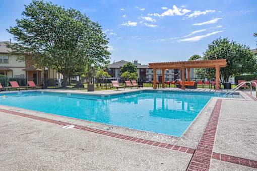 A large swimming pool with a red brick border and a wooden pergola.