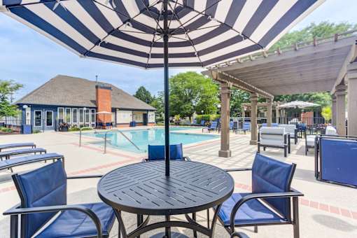 A black and white striped umbrella shades a table and chairs by a pool.