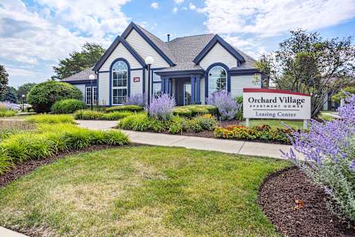 A blue and white house with a sign that says Orchard Village Apartment Homes.
