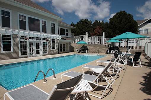 A pool with chairs and umbrellas in front of a house.