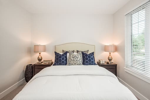 A bed with white sheets and a white headboard with blue and white pillows.