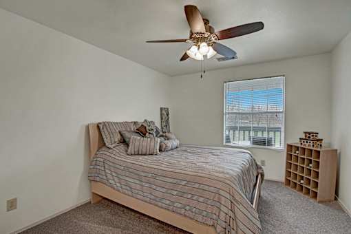 A bedroom with a bed, a ceiling fan, and a window.