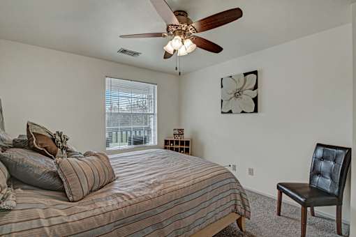 A bedroom with a bed, chair, and a ceiling fan.