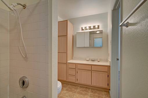 A bathroom with a white tiled shower and a wooden vanity.