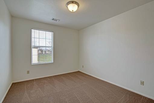 A room with a carpeted floor and a window with blinds.