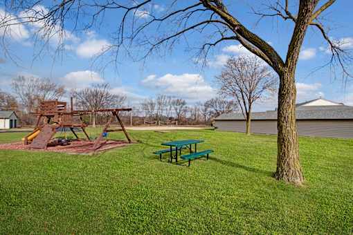 A playground with a green picnic table and a wooden swing set.
