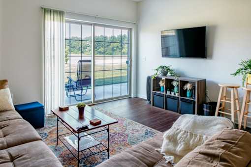 A living room with a couch, a coffee table, a TV, and a window with a view of the outside.