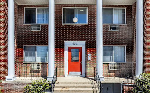 A red door is the centerpiece of a brick building with white columns.