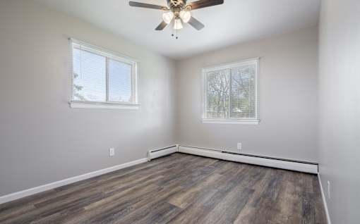 A room with a ceiling fan and two windows.