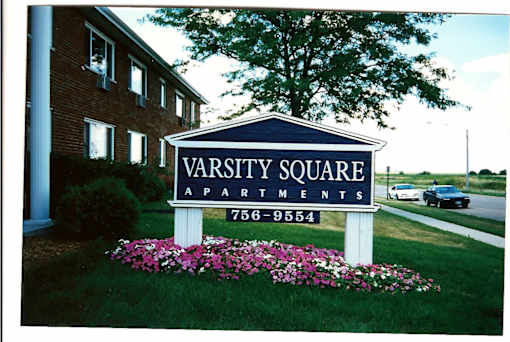 A sign for Varsity Square Apartments is in front of a brick building.