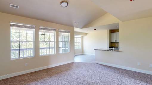A spacious room with a carpeted floor and large windows.