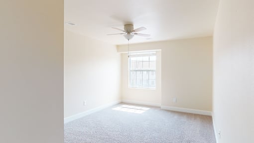 A room with a ceiling fan and a window letting in sunlight.