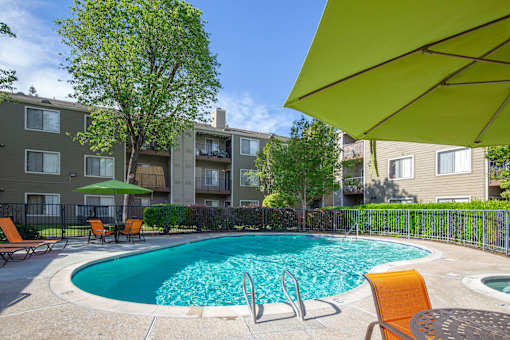 Resort-style swimming pool at Caifornia Place in gated pool area surrounded by lush greenery and blue skies for a beautiful and relaxing poolside experience