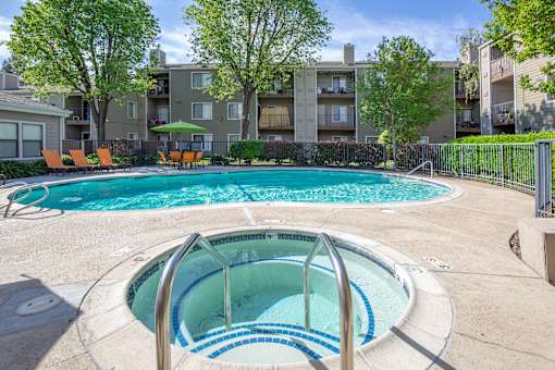 Resort-style swimming pool and serene spa at Caifornia Place in gated pool area surrounded by lush greenery and blue skies for a beautiful and relaxing poolside experience. With plenty of seating including dining tables and chaise lounges