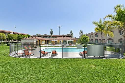 View of Azusa Gardens Pool Area inclosed by an iron fence for safety. Pool area is surrounded by lush greenery.