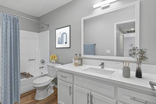 Spacious bathroom in 2 Bed 1 Bath Azusa Gardens Apartment home with wood-style plank flooring, large vanity, white shaker cabinets, quartz countertops, brushed nickel finishes, and a large shower/tub