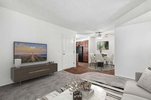 Spacious living room in 2 Bed 1 Bath Bent Tree apartment home with carpeted flooring and open concept layout leading to dining nook and kitchen area. Dining nook and kitchen have plank wood-style flooring.
