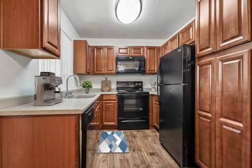Kitchen in 2 Bed 1 Bath Bent Tree Apartment home with wood-style plank flooring, cherry wood cabinets, black appliances, and plenty of storage space for all of your needs!