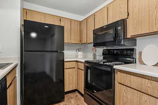 Kitchen in 2 bed 2 Bath Bent Tree apartment with wood plank-style flooring, light wood cabinets, black appliances, and plenty of storage for all of your needs!