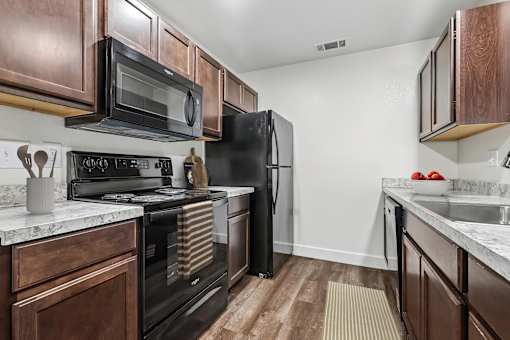 Kitchen in 2 Bedroom 1 Bath Option B Bent Tree Apartment with wood plank-style flooring, dark wood cabinets, black appliances, and modern marbled countertop.