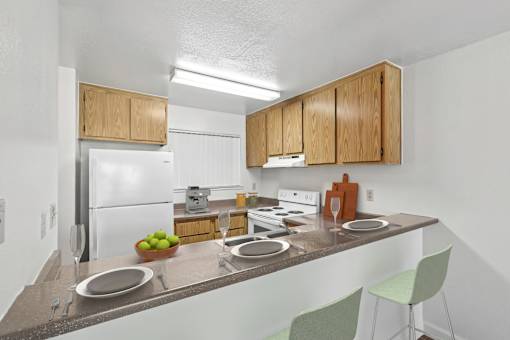 Kitchen with bar top seating in 1 Bed 1 Bath B apartment home at California Place apartments with light wood cabinetry and white appliances